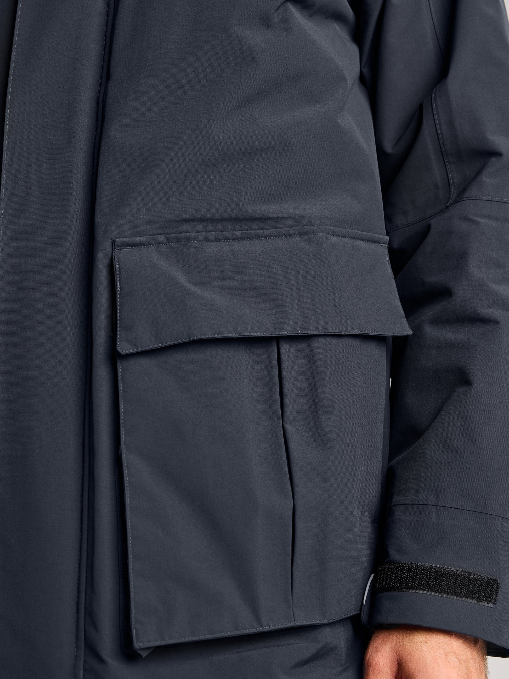 Close-up of an ACT ETNZ LONG PARKA sleeve and pocket by SLAM. The waterproof parka boasts a large flap pocket and adjustable Velcro cuffs, providing warm comfort. A portion of an arm wearing the parka is visible.