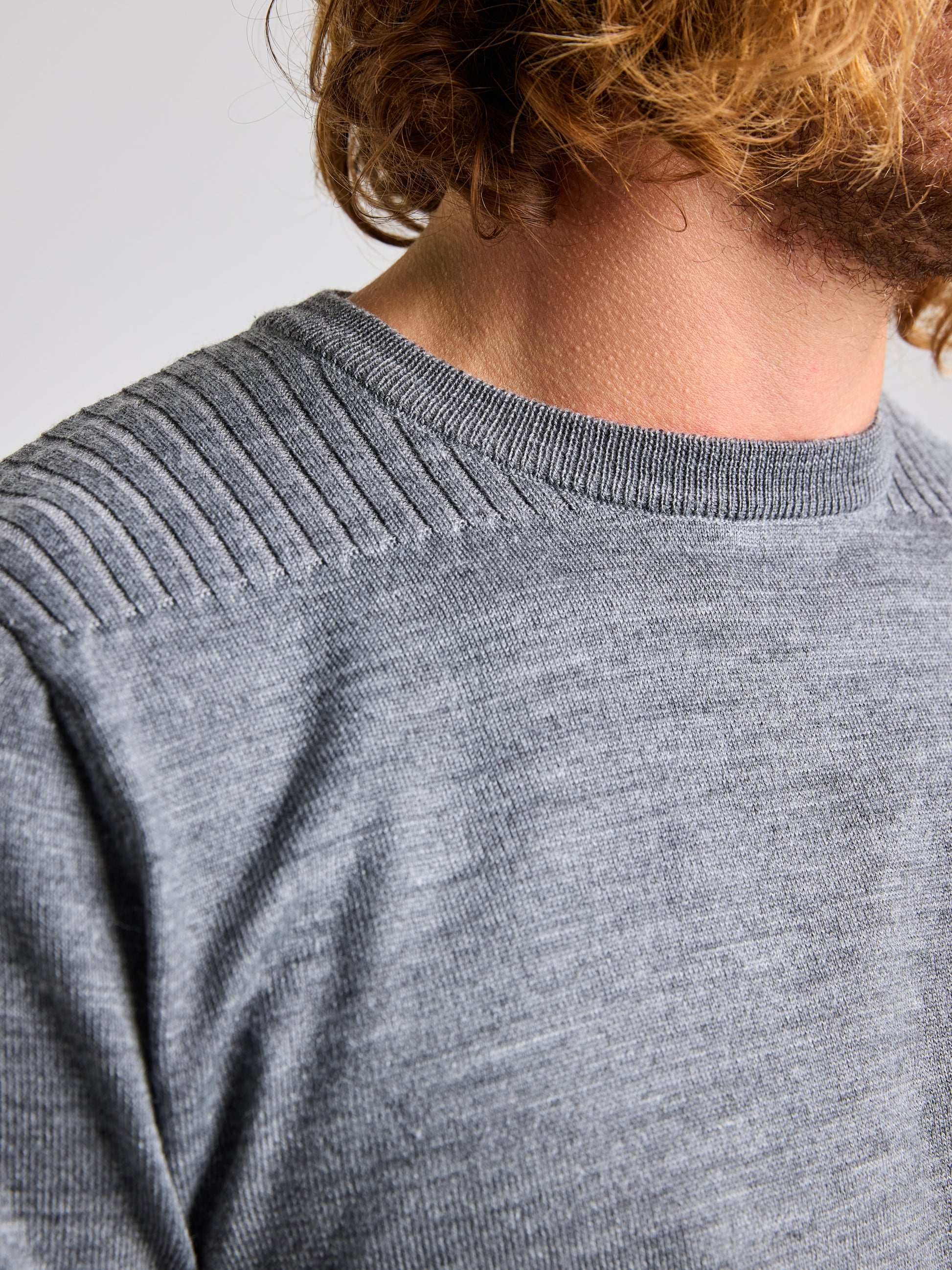 A close-up image showcases a person wearing the SEAWOOL CREWNECK by SLAM, a gray knit sweater featuring ribbed detailing on the shoulders. Crafted from a Merino-blend yarn, the photo focuses on the upper torso and part of the neck area, emphasizing the texture of this regular fit piece against a neutral and out-of-focus background.