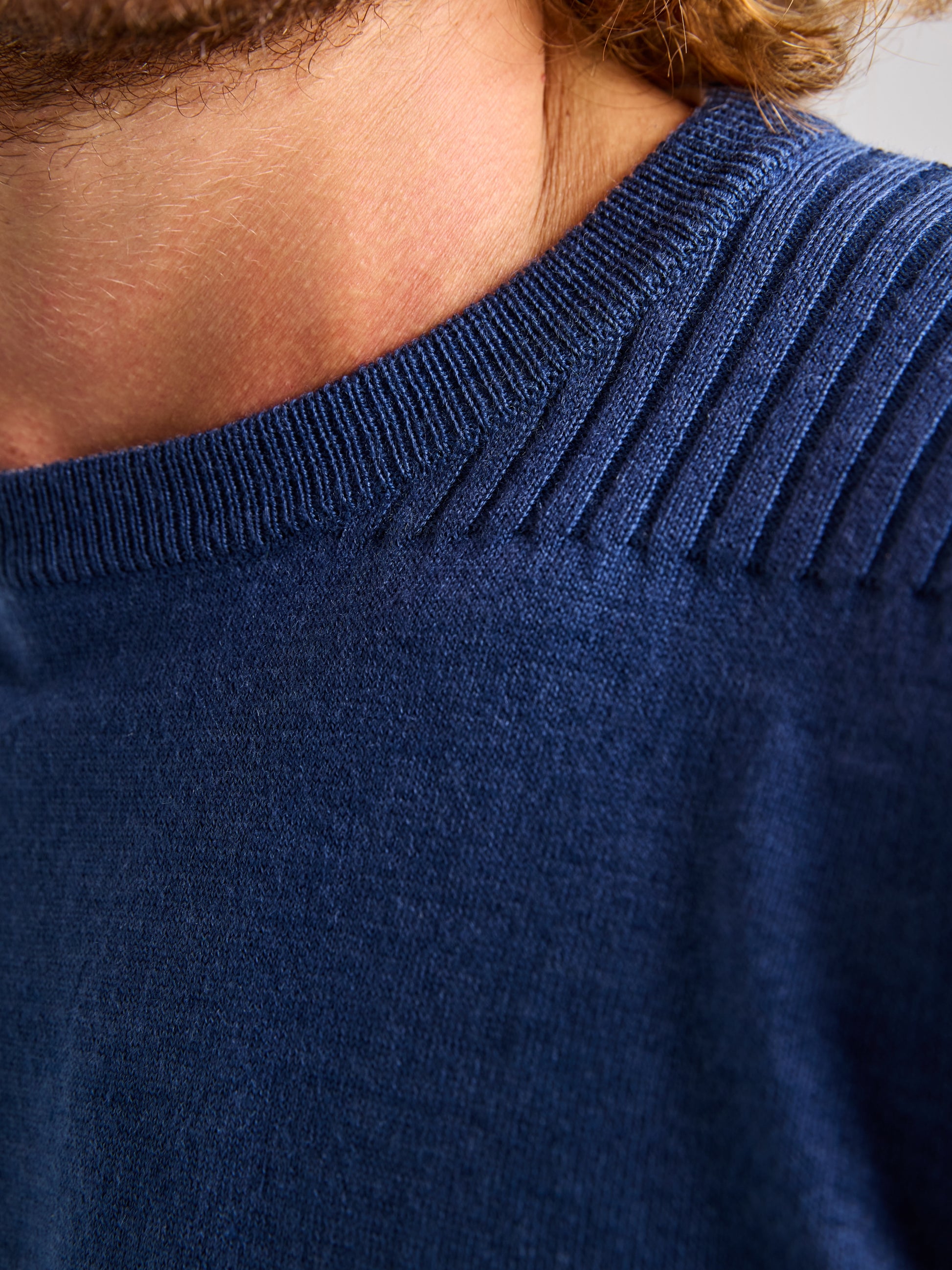 Close-up of an individual wearing a blue SLAM SEAWOOL CREWNECK sweater featuring ribbed detailing along the neckline. Only part of the neck, collarbone, and shoulder are visible.