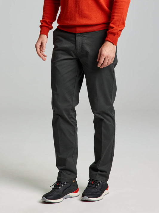 A person dressed in a bright orange sweater, DECK CHINO PANT CL by SLAM in GRAPHITE, and black sneakers with red accents is standing against a neutral background. The image emphasizes the comfortable sporty fit while keeping the person's face hidden.