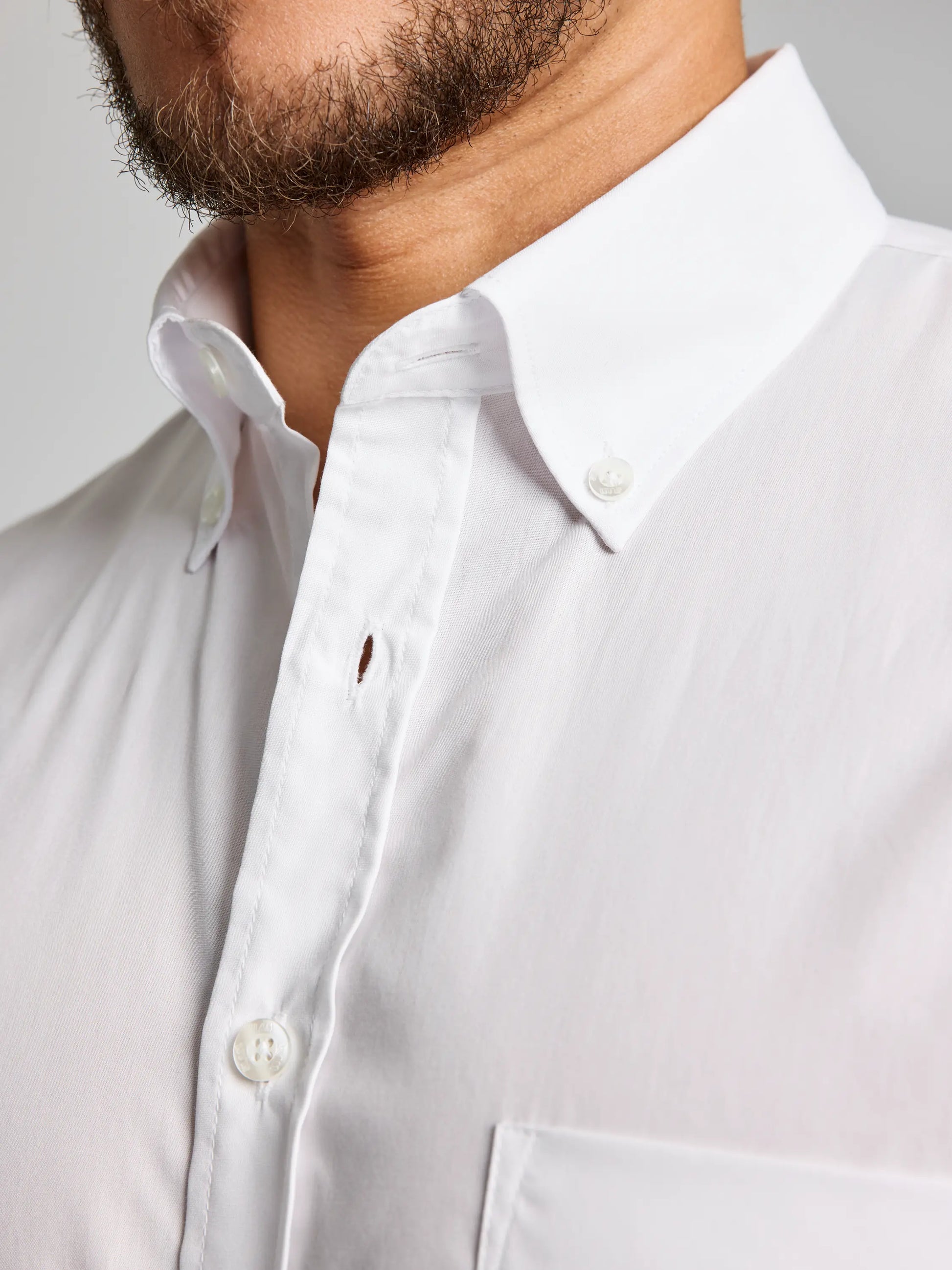 A close-up of a person wearing the SLAM DECK NO IRON SHIRT CL, featuring a button-down collar with one missing button in the middle. The design highlights the upper part, including the collar and chest pocket. This no-iron shirt from SLAM blends style with convenience for an effortlessly polished appearance.