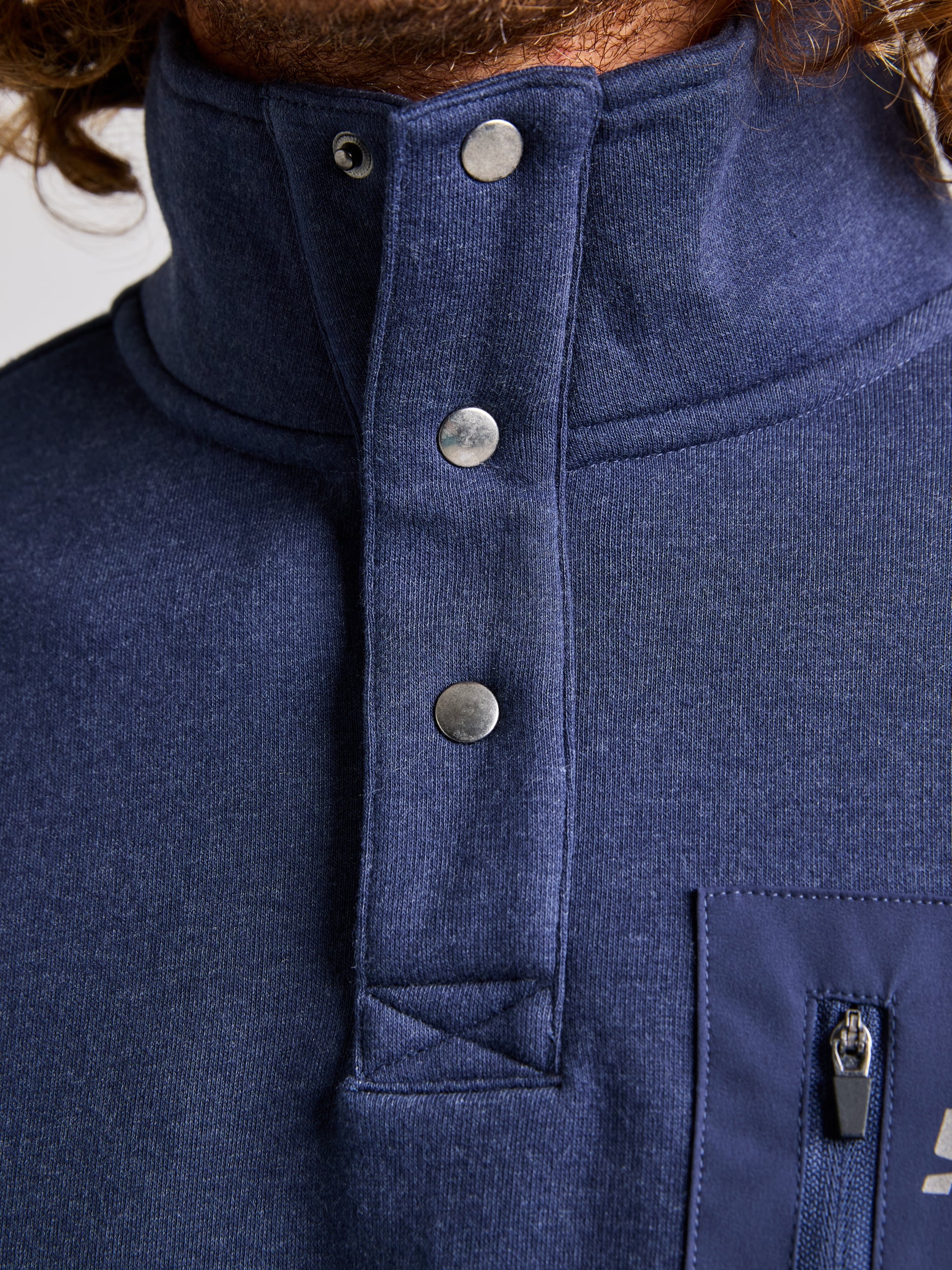 Close-up of a person wearing the navy blue SWEATSHIRT ANAPO CL by SLAM. The men's sweatshirt boasts a high collar with a 4-button opening and includes a zippered chest pocket. The fabric exhibits a textured appearance, with long hair visible near the collar.