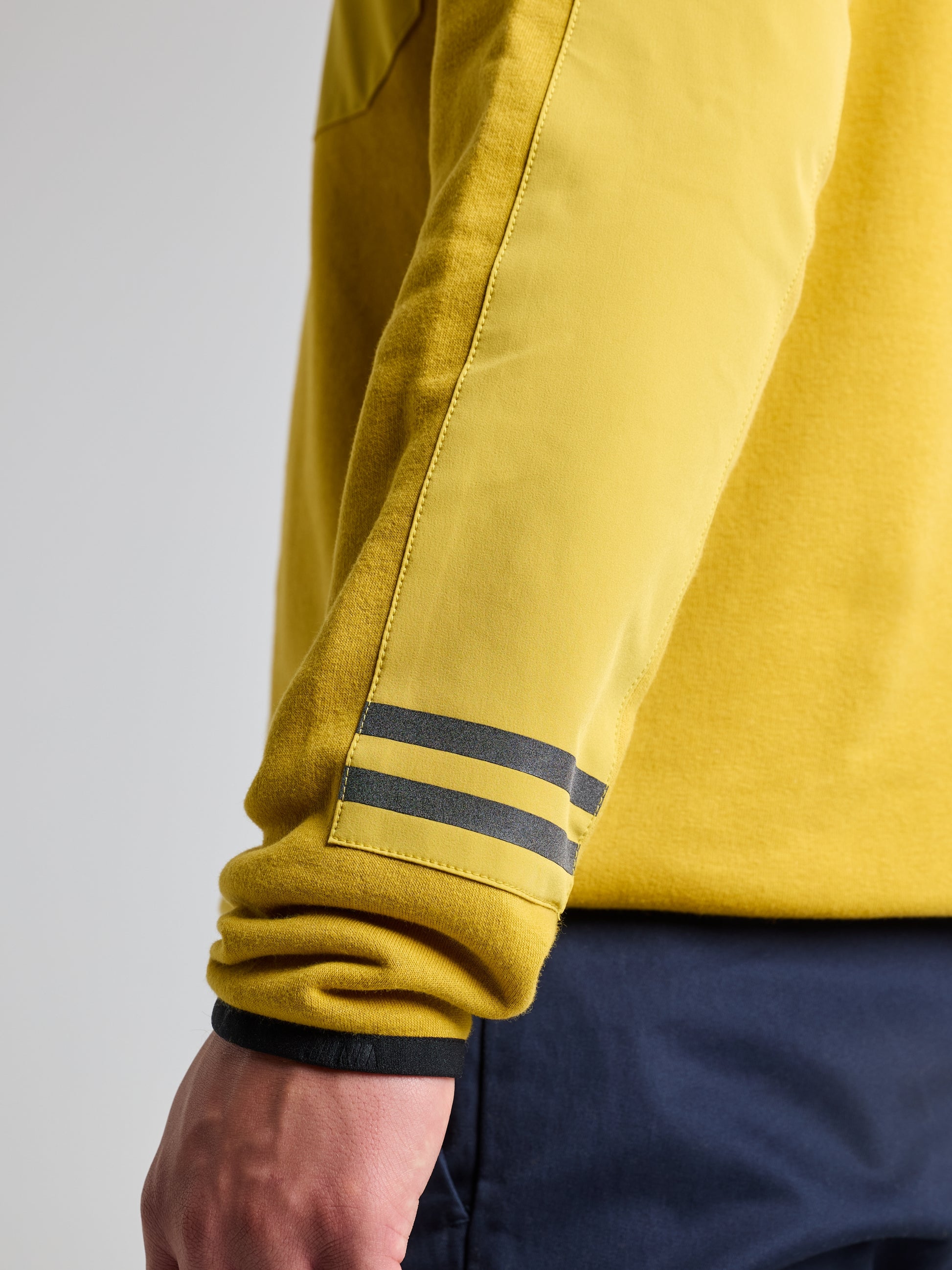 A close-up of a person wearing the SLAM SWEATSHIRT ANAPO CL, featuring two dark horizontal stripes near the cuff. The high collar and 4-button opening add subtle detail, with the person standing with their arm relaxed by their side against a plain light gray background.