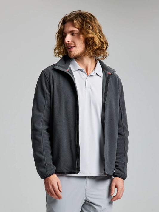 A person with long curly hair is wearing a GRAPHITE DECK FLEECE CL by SLAM over a light gray collared shirt. They are standing against a plain light background and are looking to the side.