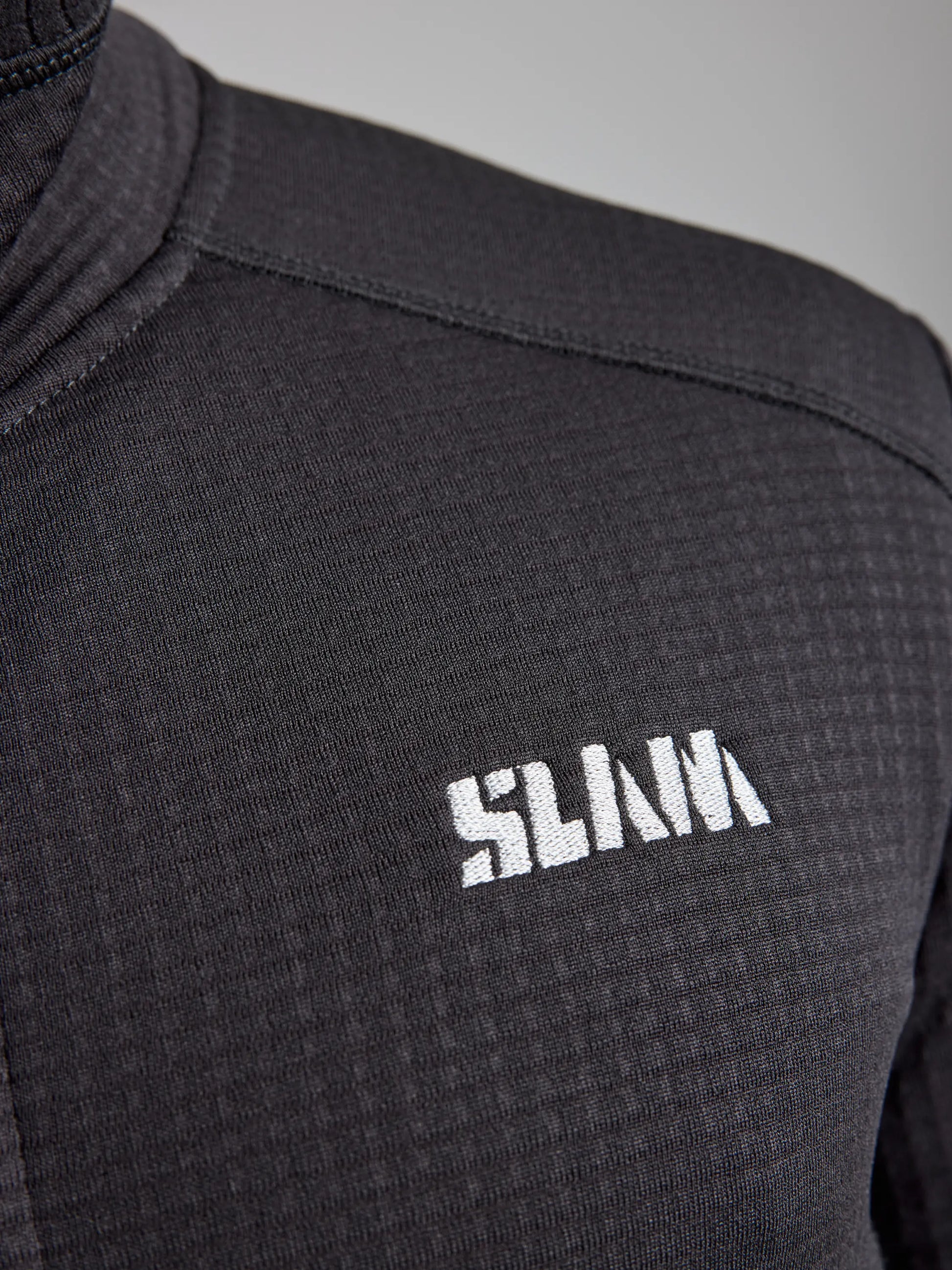 Close-up of a black textured fabric with a high collar, showcasing the word "SLAM" in white, stylized block letters on the left side. The ACTIVE GRID FLEECE design incorporates heat-regulating technology for optimal comfort.