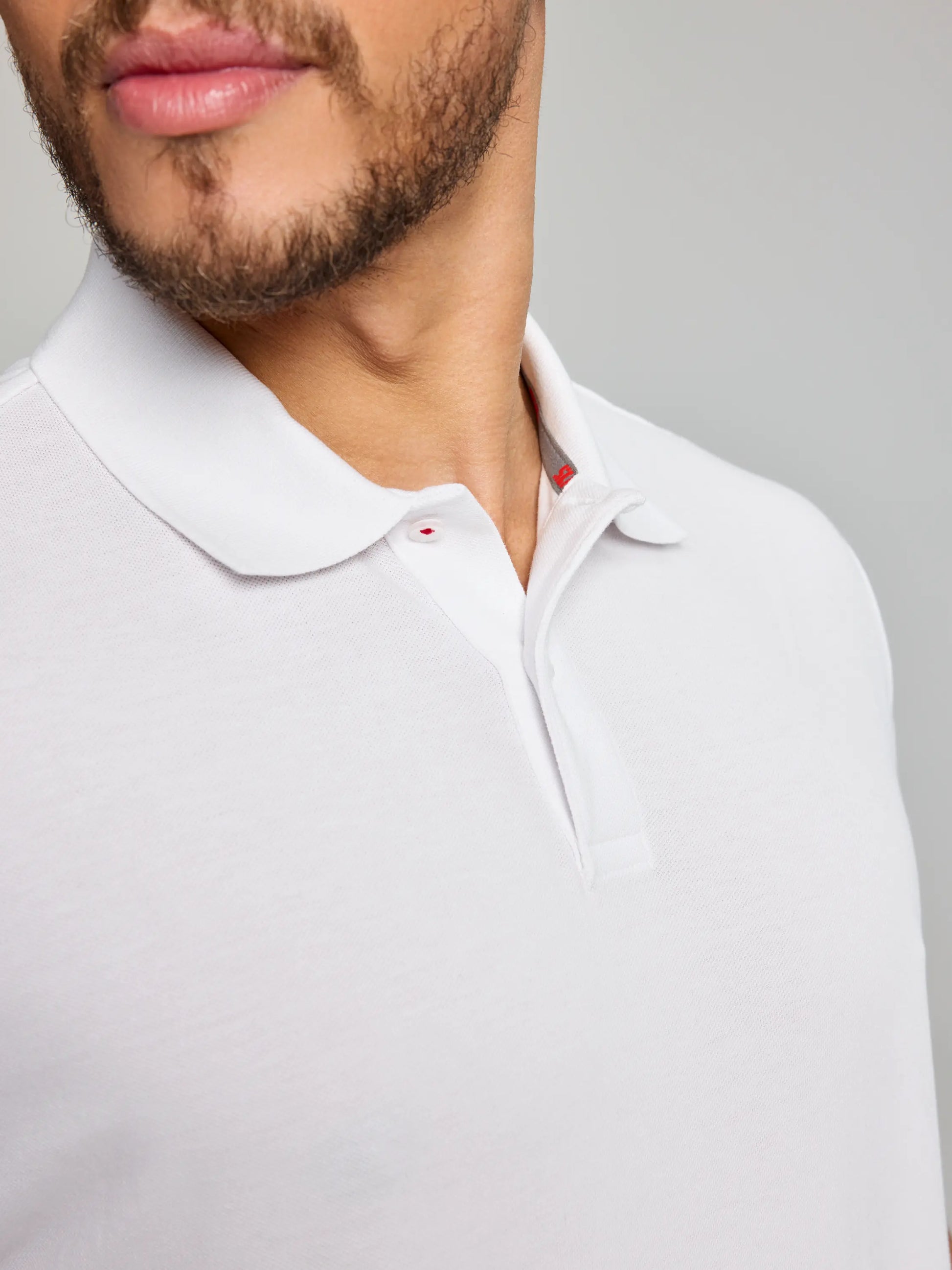 A person wearing the SLAM DECK POLO SHORT SLEEVE CL is partially visible. The focus is on the shirt's lightweight cotton pique texture and collar against a plain background. The person's face is partially visible, with emphasis on the mouth and beard area.