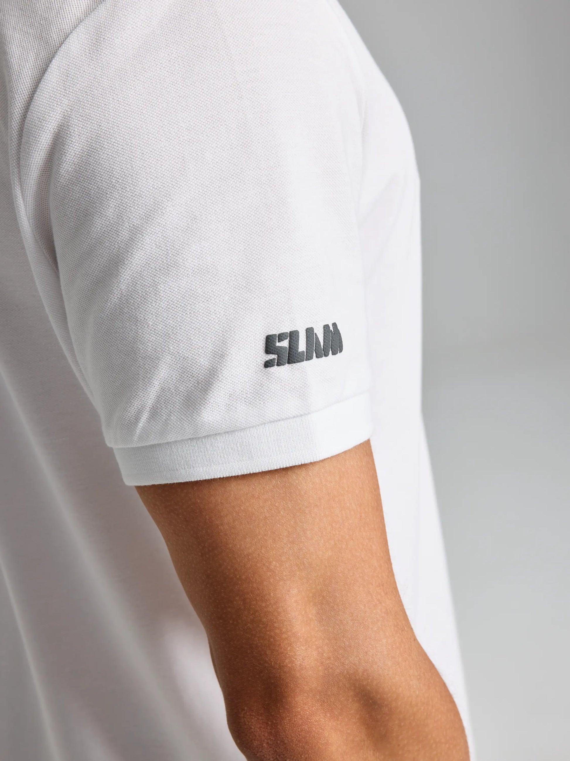 A person is wearing the SLAM DECK POLO SHORT SLEEVE CL, featuring a small black logo on the sleeve. The slim fit design accentuates the wearer, set against a plain, neutral background.