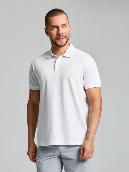 A man with short hair and a beard stands against a plain background. He is wearing the SLAM Deck Polo Short Sleeve CL in bright white and light gray pants, his gaze directed to the side with a neutral expression.