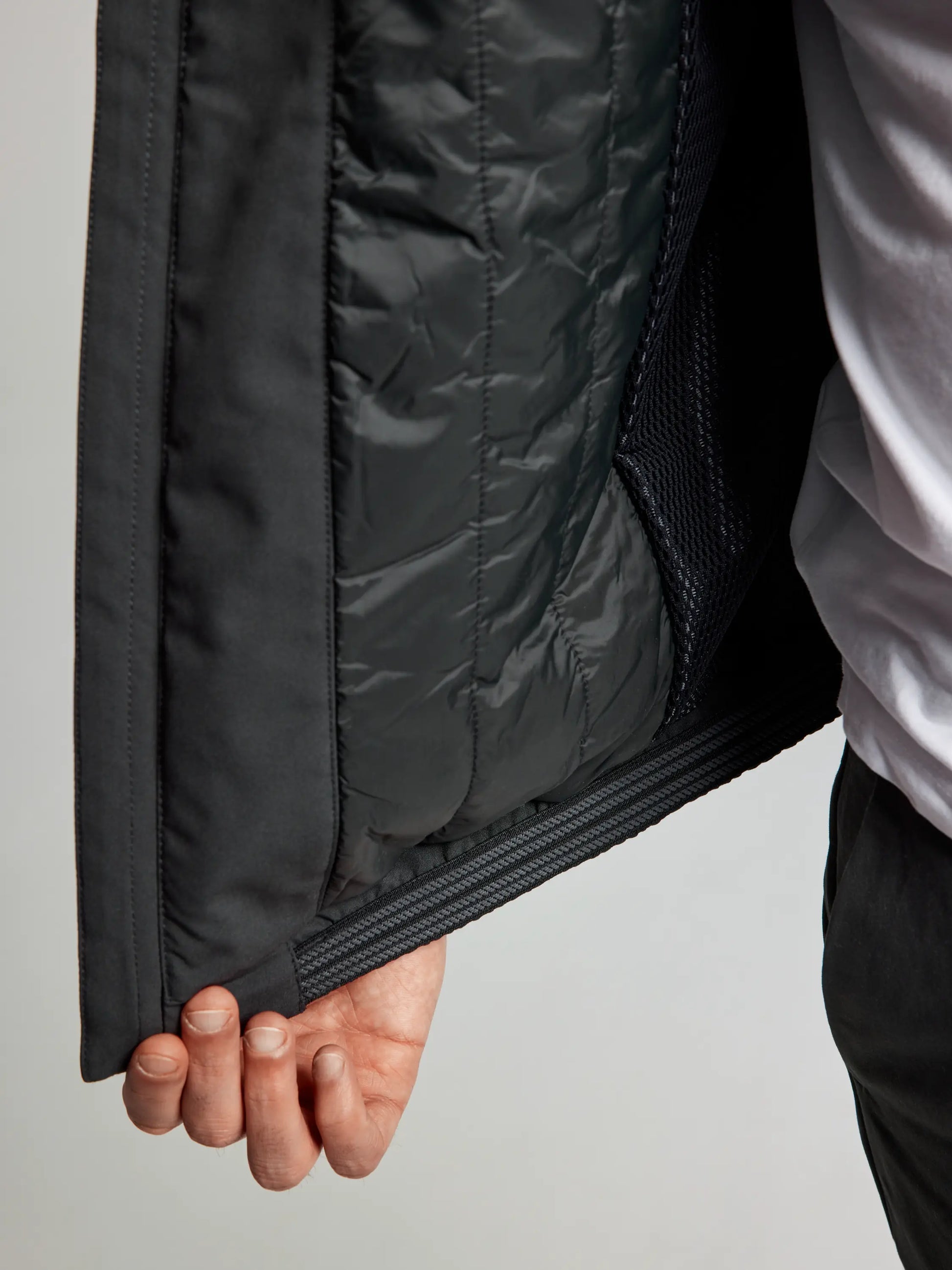 A person showcases the interior of the DOCK INSULATED JACKET CL by SLAM, revealing its quilted lining and mesh pocket. The individual in a white shirt highlights the fleece-lined collar, ideal for extra warmth and comfort.