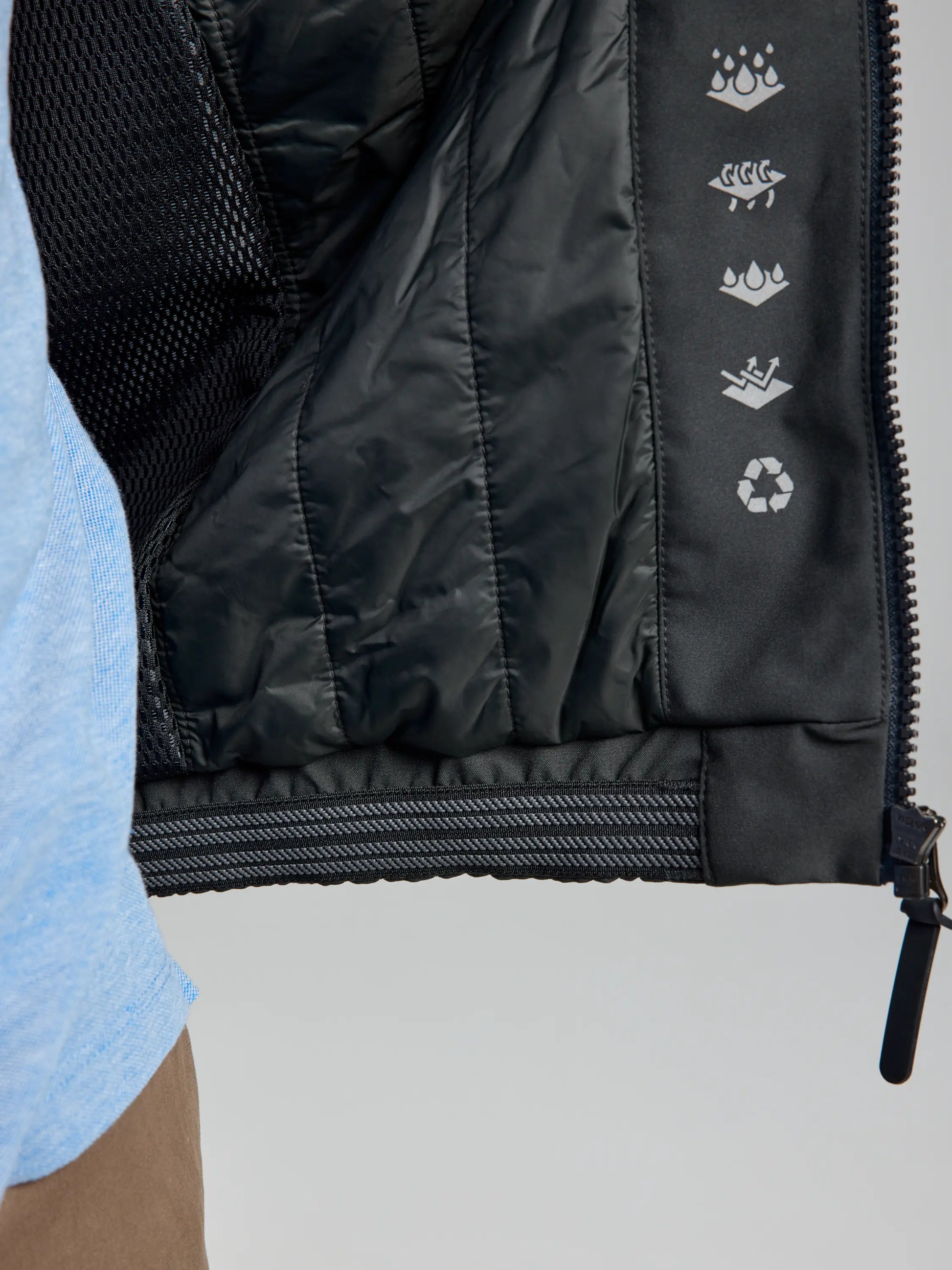 Close-up of the DOCK INSULATED JACKET CL interior by SLAM showcasing five icons: water droplets, fish skeleton, feather, hand washing, and recycling symbol. The partially zipped jacket reveals its black quilted lining and fleece-lined collar over a light blue shirt beneath.