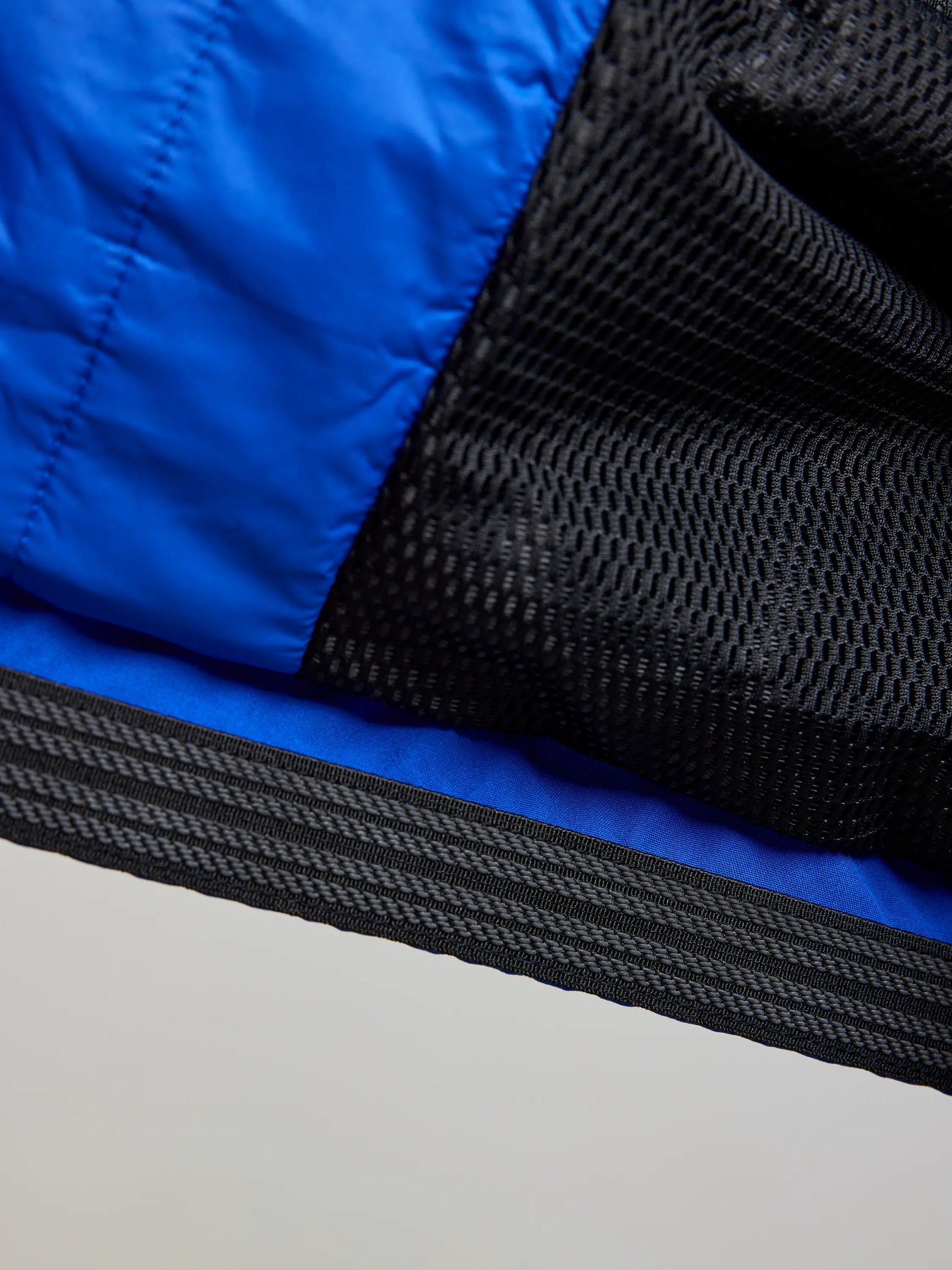 Close-up of the DOCK INSULATED JACKET CL by SLAM, featuring a blue fabric with a black mesh overlay. The men's nautical winter jacket showcases a striped black band at the edge, with textures and stitching clearly visible to highlight the contrast between the smooth fabric and its waterproof, porous mesh.