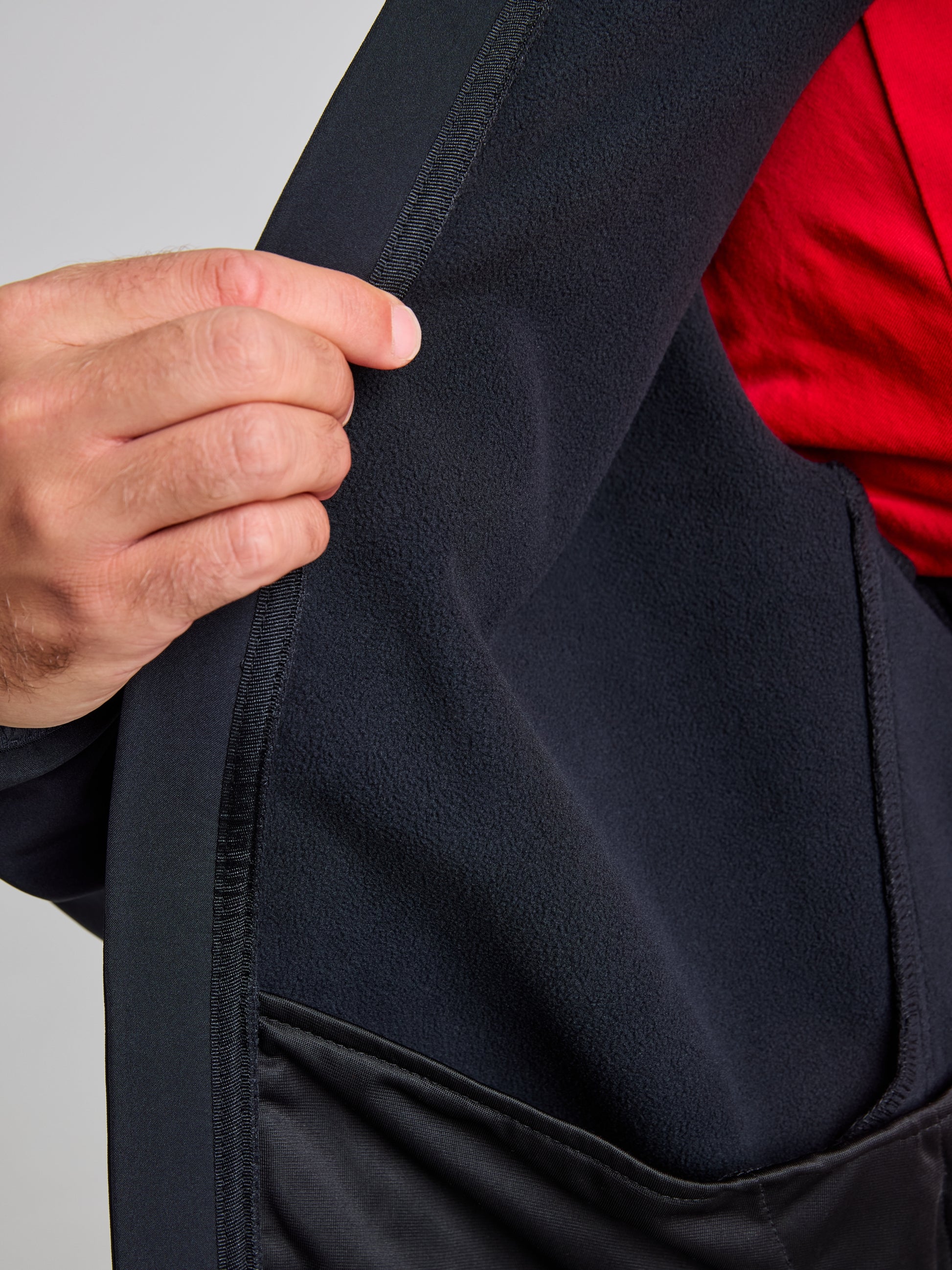 A person is holding open an ACTIVE WARM SOFTSHELL JACKET by SLAM, revealing its soft and breathable inner lining. A hint of a red garment worn underneath can be seen.