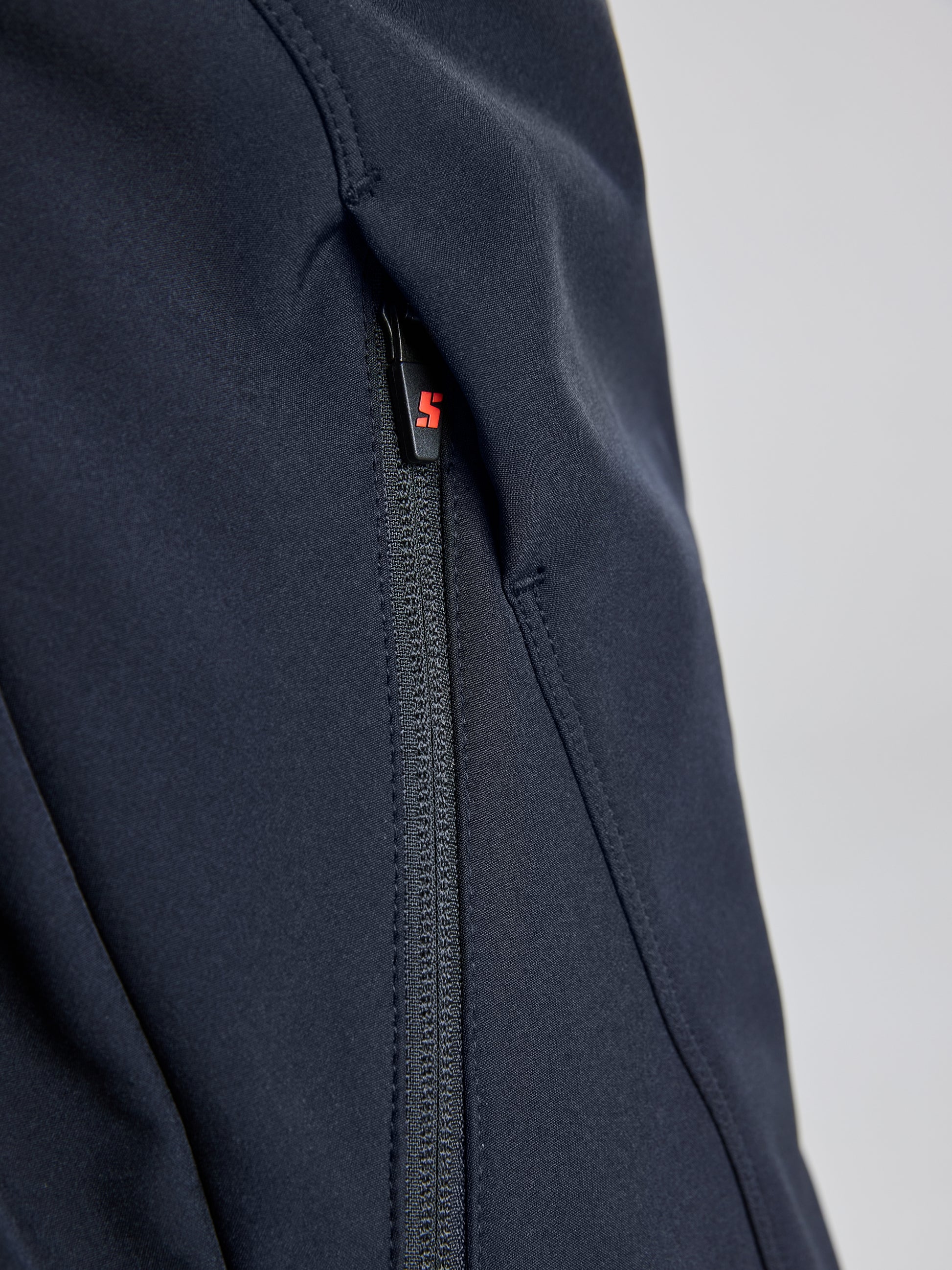 A close-up of the ACTIVE WARM SOFTSHELL JACKET by SLAM reveals navy blue fabric, characterized by its waterproof quality. It features a black zipper with a subtle red detail on the pull. The breathable material displays visible seams and stitching, making it an ideal choice for versatile weather conditions.