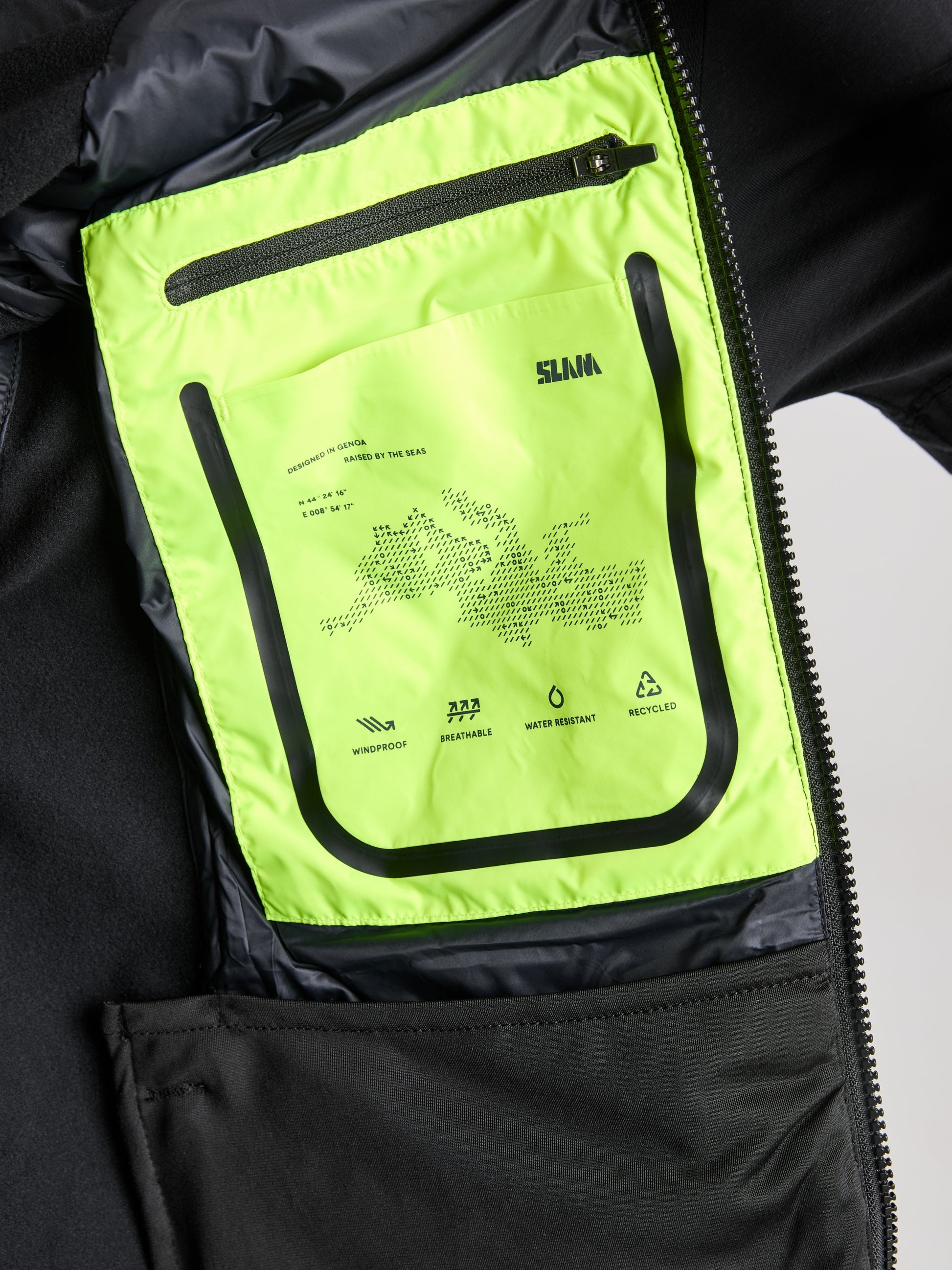 A close-up view of the inside of the HYBRID SOFTSHELL JACKET by SLAM reveals a bright green label detailing its breathable and waterproof materials. The label also includes information about water resistance and recycled content, highlighted with a small map outline graphic.