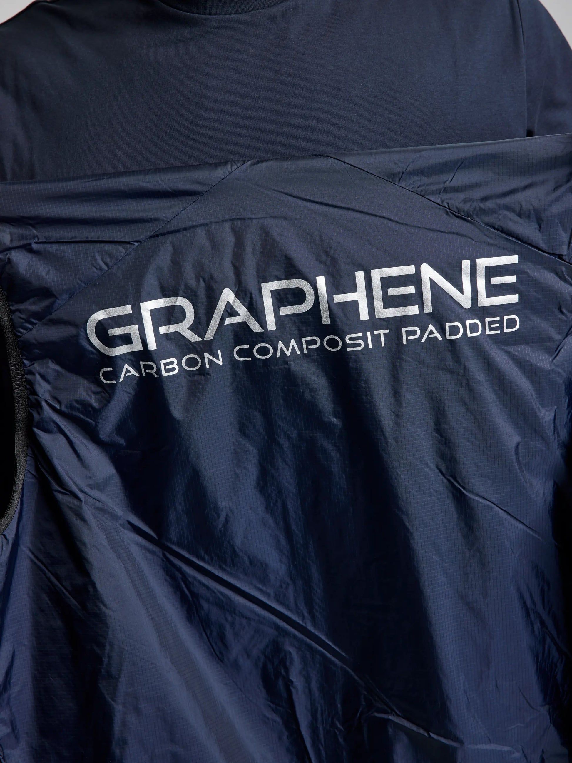 Close-up of a dark blue men's gilet, featuring the "ACTIVE GRAPHENE RSTOP VEST" by SLAM, with "GRAPHENE CARBON COMPOSITE PADDED" in white on the back. Made from recycled Nylon Ripstop, the fabric provides a smooth, slightly shiny texture that complements its innovative design.