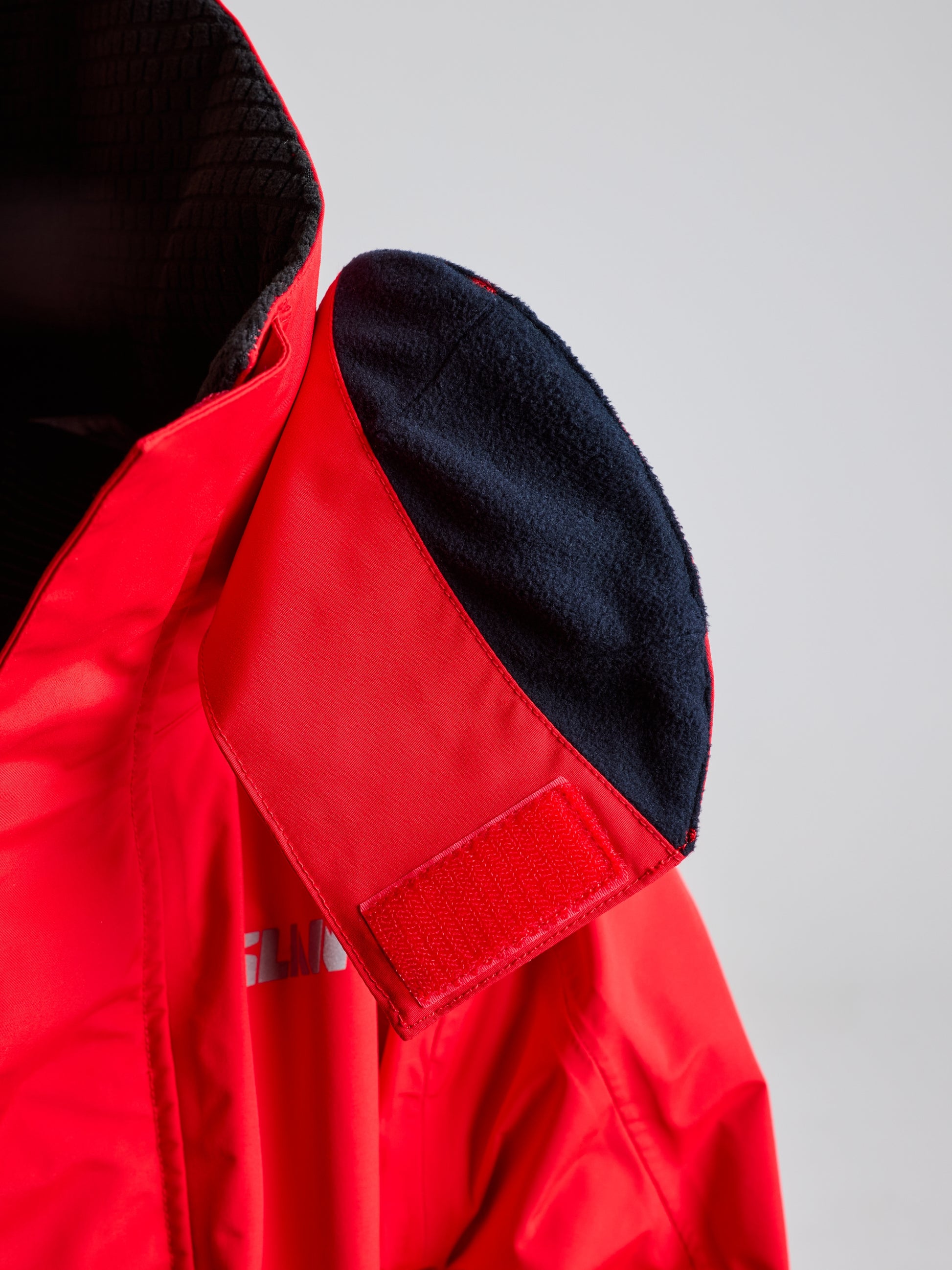 A close-up of the SLAM PRO OFFSHORE JACKET highlights its collar, which is partially turned inside out. The inner lining features a soft black fabric. A Velcro patch indicates that it can be securely fastened, enhancing its waterproofing capabilities for additional protection against the elements.