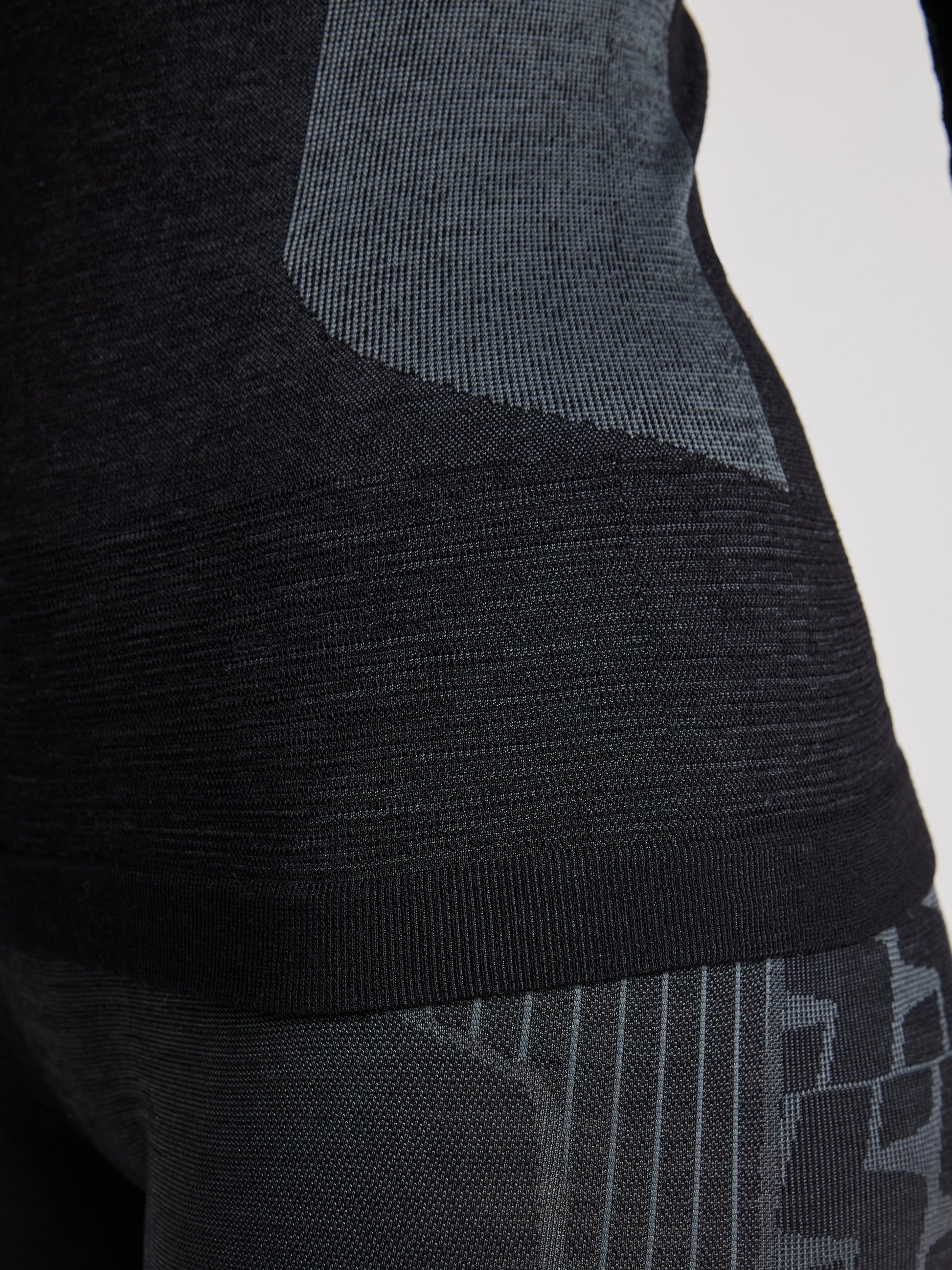 Close-up of a person wearing the SLAM PRO SEAMLESS MERINO TOP and textured leggings. The focus is on the midsection and part of the leg, highlighting the ergonomic fit and quick-to-dry fabric's pattern.