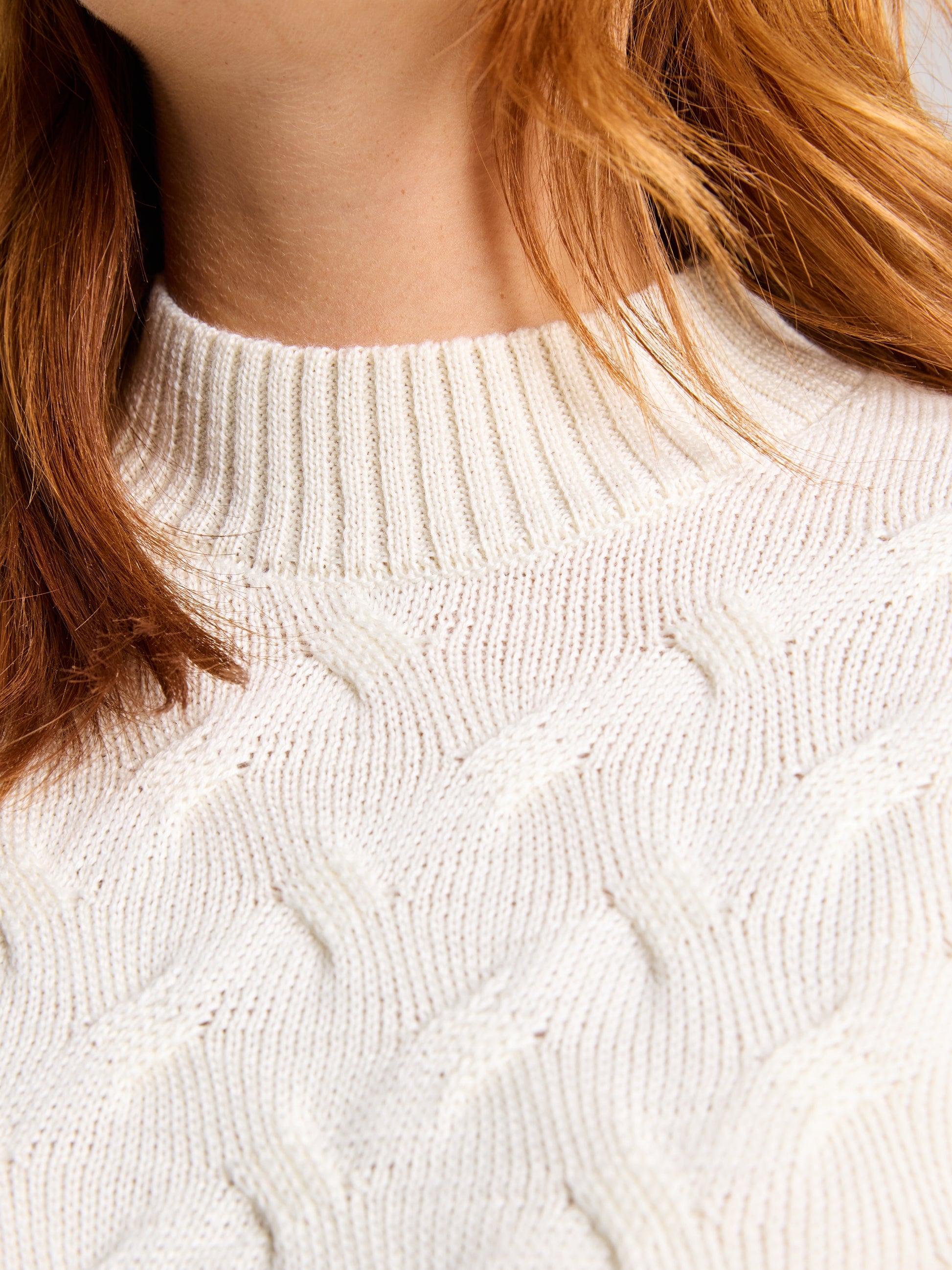 Close-up of a person wearing the SEAWOOL WOMAN CABLE JUMPER by SLAM. The focus is on the textured pattern of the Merino-blend yarn, with strands of red hair visible near the neckline.