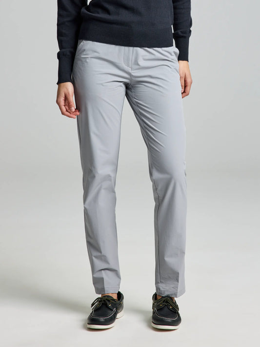 A person wearing an aluminium WOMAN TECH CHINO PANT CL by SLAM stands against a plain background. They are also wearing black boat shoes with white soles. The image focuses on the lower half of the body, highlighting the sleek design of these lightweight technical trousers.