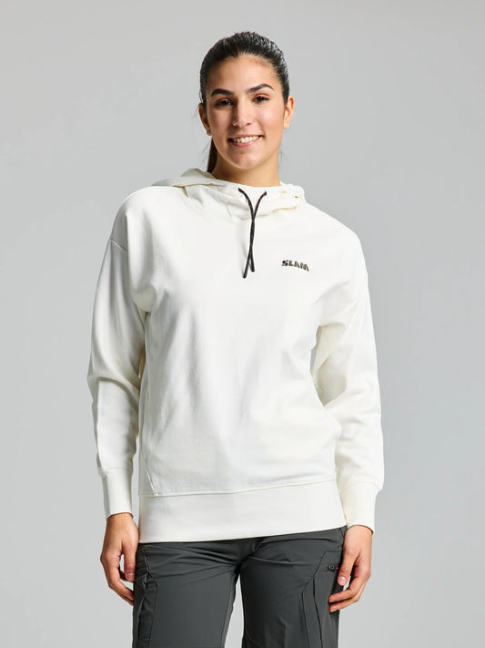 A person wearing the SLAM DECK WOMAN HOODIE CL in off white, featuring a small logo on the left chest and black drawstrings, paired with dark gray pants. They are smiling and standing against a plain gray background.