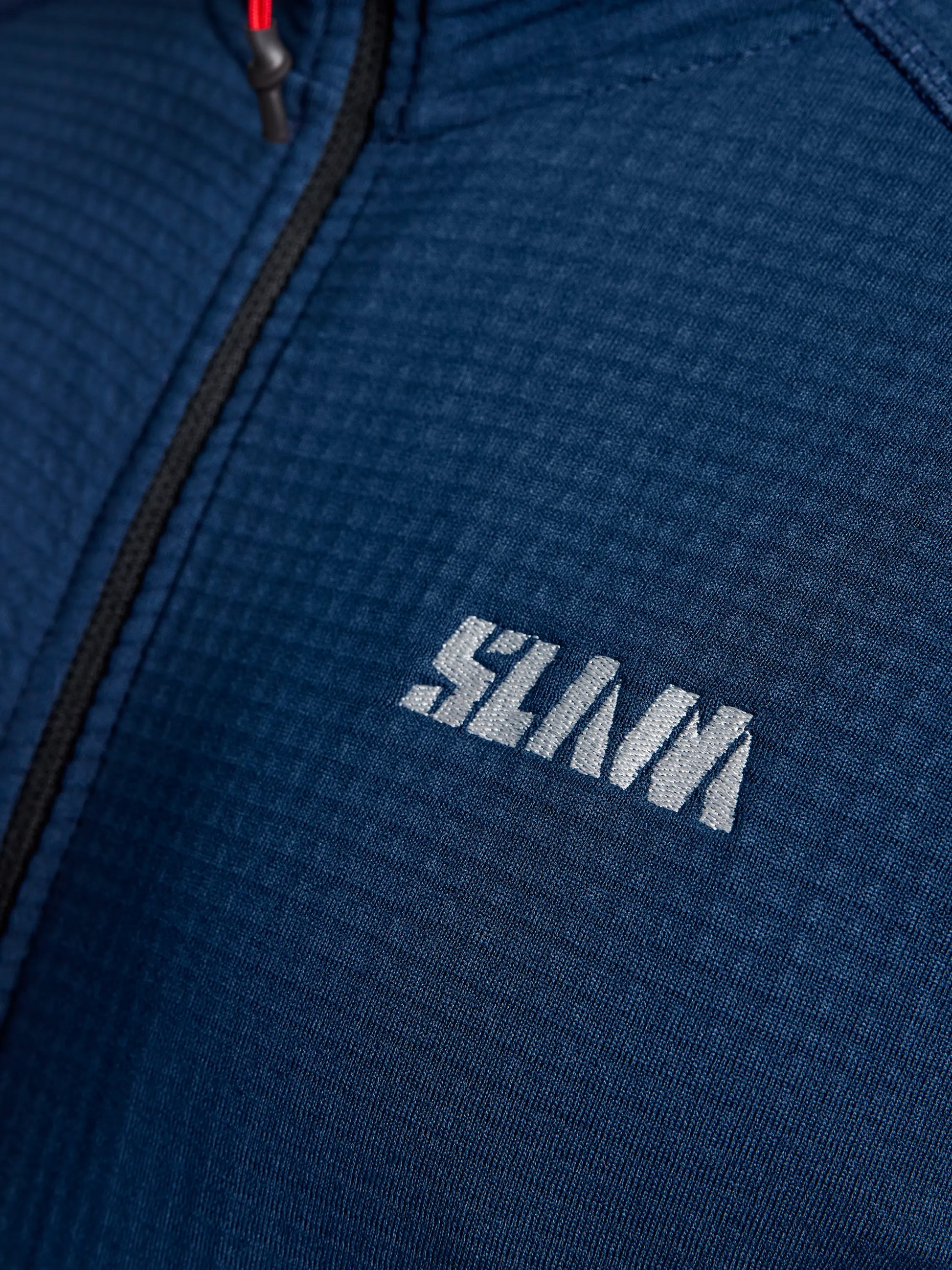 Close-up of the blue textured fabric of SLAM's ACTIVE WOMAN GRID FLEECE CL, featuring a zipper and the logo "SLAM" in white letters. The breathable material showcases a distinctive grid-like pattern from Pontetorto's Grid Fleece.