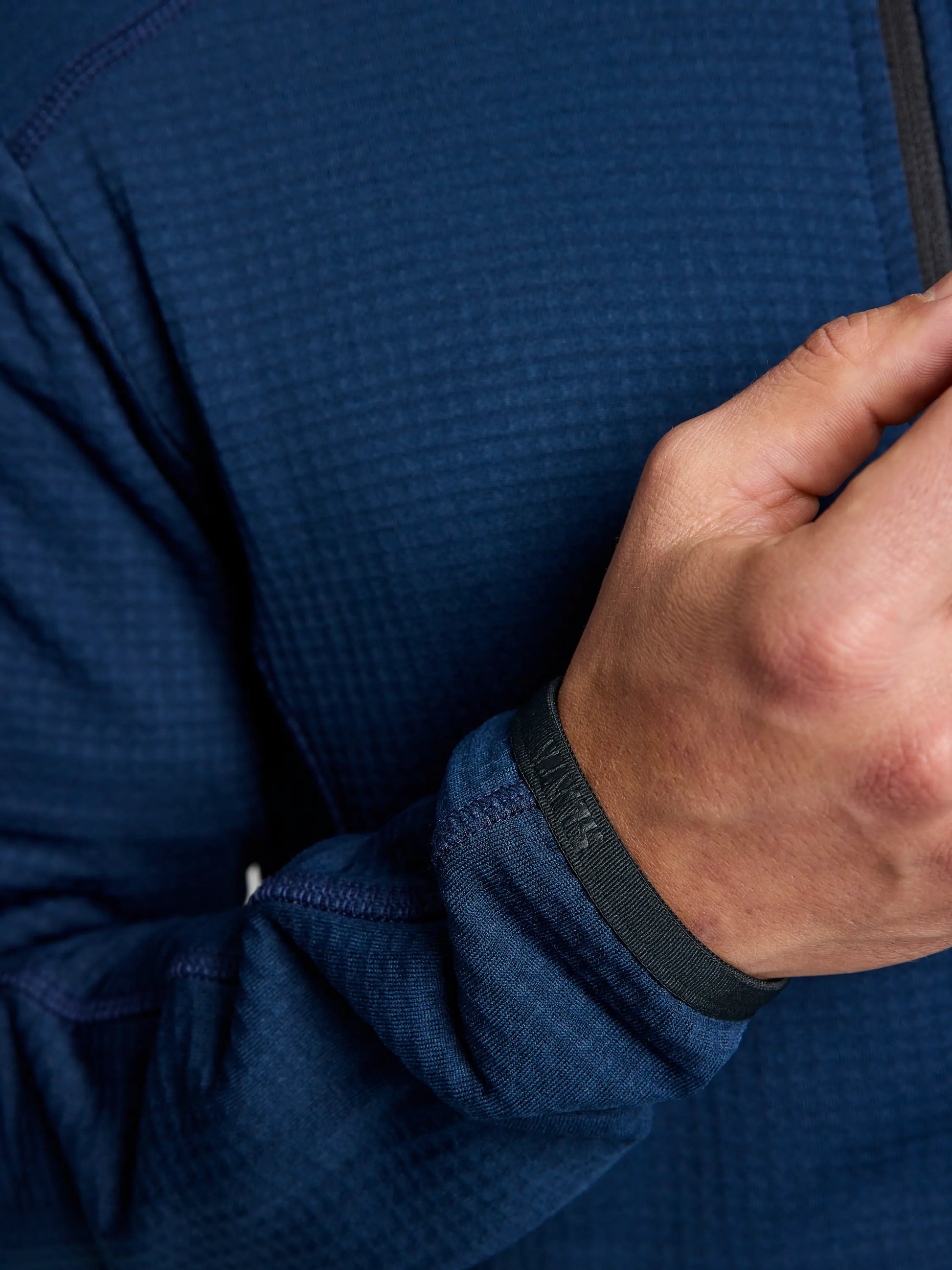 A person adjusts the ACTIVE WOMAN GRID FLEECE CL, a textured blue long-sleeve shirt from SLAM, featuring thumb holes. The focus is on the hand and fabric, highlighting the breathable design and material made from Pontetorto's Grid Fleece.