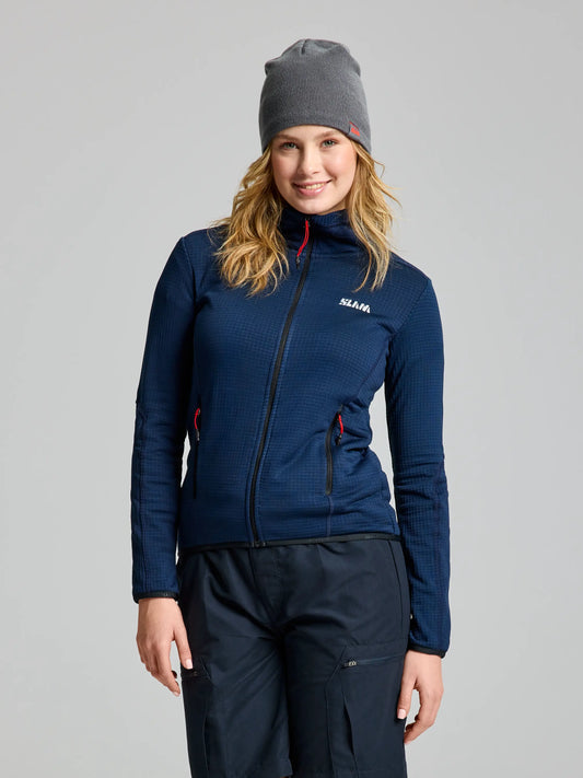 A person wearing a DARK NAVY ACTIVE WOMAN GRID FLEECE jacket by SLAM, paired with a gray beanie and dark pants, stands against a neutral background. They have long hair and are smiling slightly. The breathable material of the jacket ensures they stay comfortable in any weather.