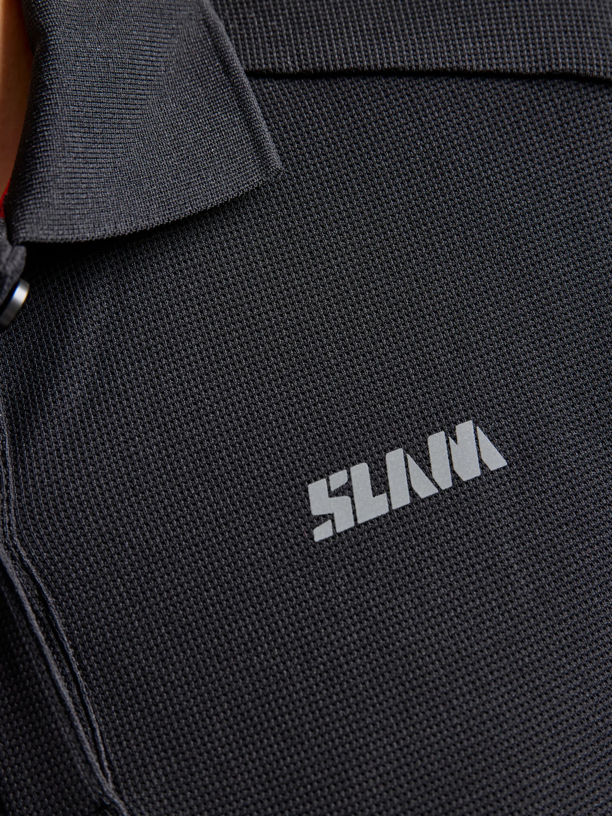 Close-up of a textured black Tactel fabric polo with a collar, featuring the word "SLAM" in white uppercase letters on the chest area. This quick-drying WOMAN LOGO TACTEL POLO CL provides excellent sun protection, making it both stylish and functional.