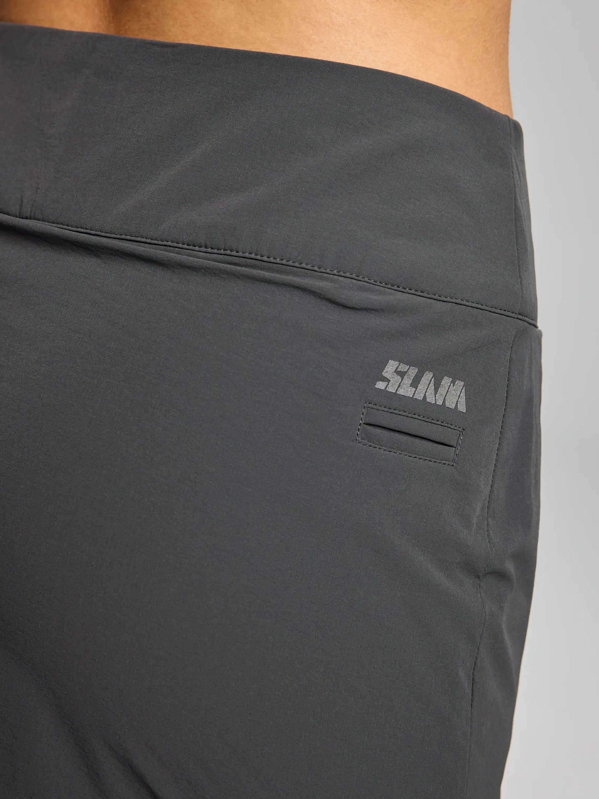 Close-up of a person wearing the TECH WOMAN SKORT CL by SLAM in dark gray, featuring a small "11AMA" logo on the side. The minimalist design and lightweight nylon stretch material ensure practicality, making them ideal for any active woman's wardrobe.